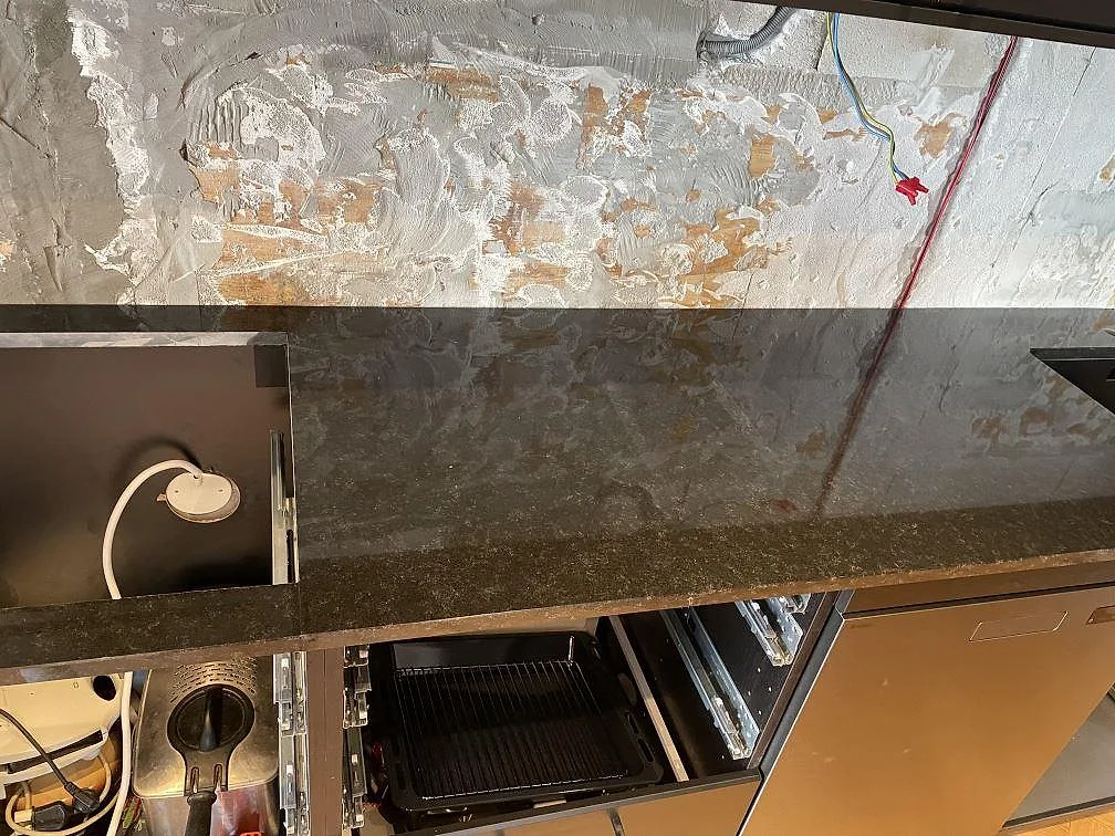 Lång köksbänkskiva i polerad Nero Assoluto granit med diskho, öppna skåpstommar och exponerad vägg i Kävlinge.