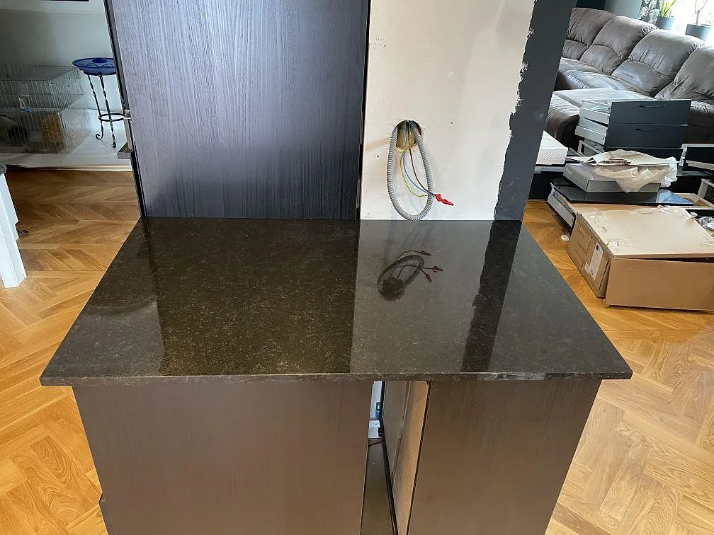 Polerad svart Nero Assoluto granit som peninsula med fiskbensgolv och mörka skåpstommar i ett kök i Kävlinge.