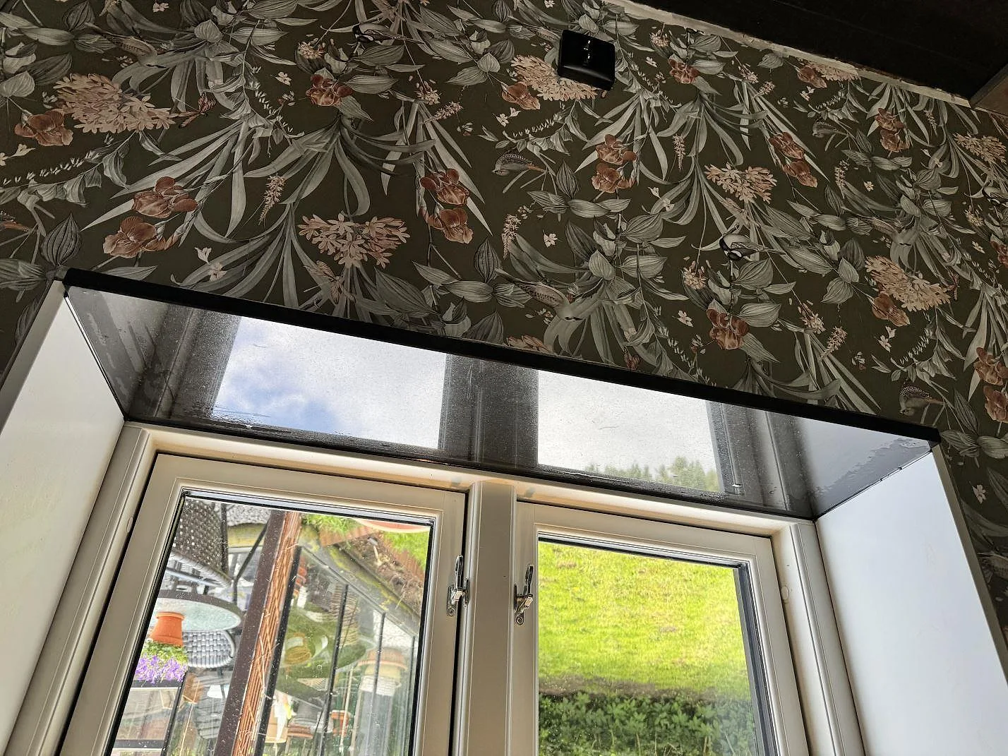 Blank fönsterbänk i Nero Assoluto granit med floral vägg ovanför ett köksfönster i Kävlinge.