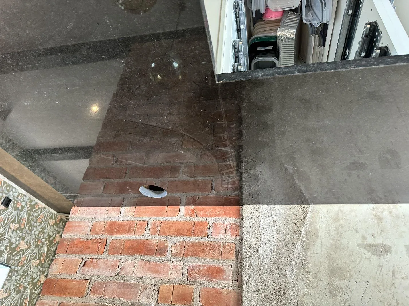 Detalj av polerad Nero Assoluto granit vid exponerad tegelvägg och öppen köksförvaring i Kävlinge.