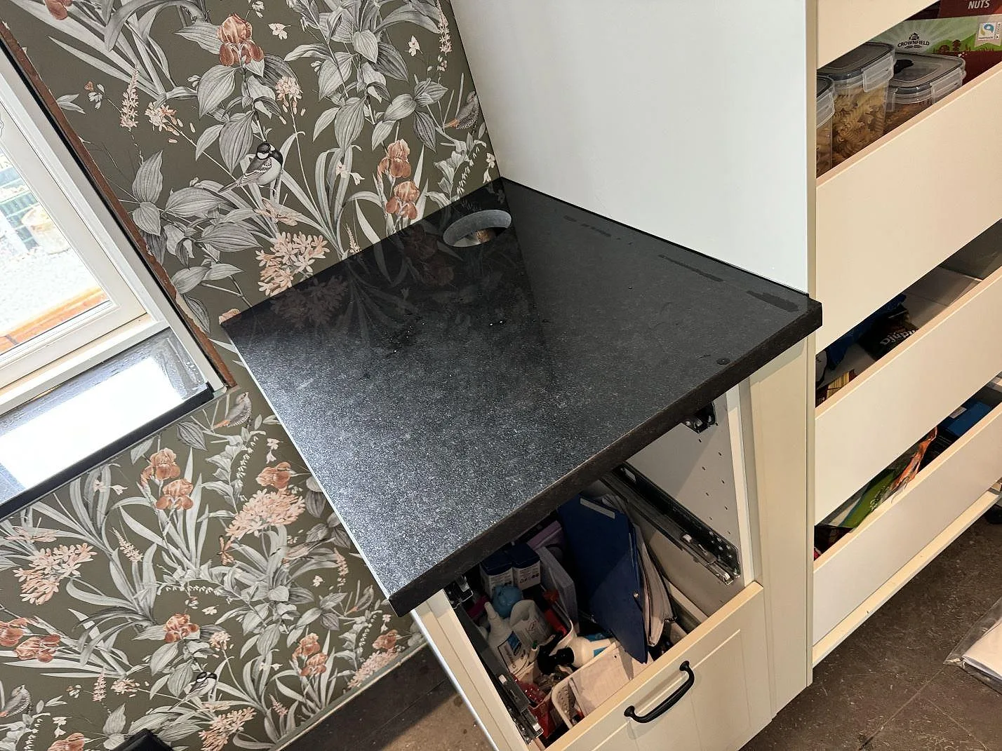 Polerad bänkskiva i Nero Assoluto granit vid floral tapet och vit förvaring i Kävlinge.