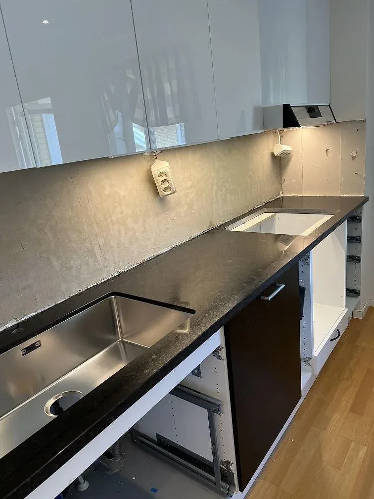 Köksbänkskiva i polerad Nero Assoluto granit med underlimmad rostfri diskho och vita kakelplattor i ett kök i Kävlinge.