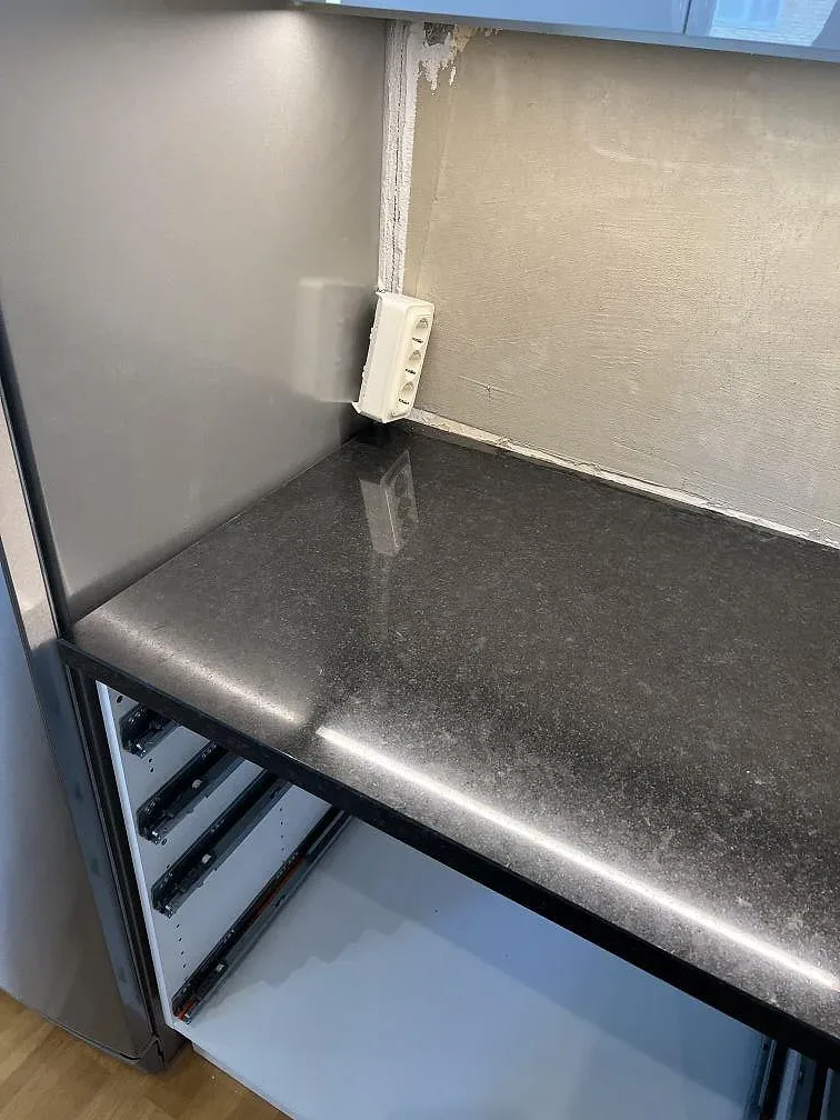 Detalj av svart polerad Nero Assoluto granit mot vit kaklad vägg och eluttag i kök i Kävlinge.
