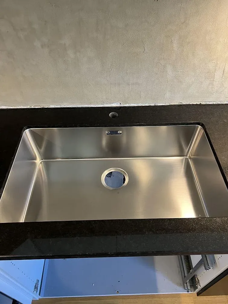 Detalj av underlimmad rostfri diskho monterad i polerad Nero Assoluto granit i kök i Kävlinge.