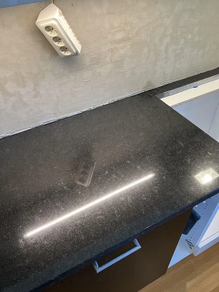 Närbild på polerad Nero Assoluto granit med LED-reflex och vit vägg under montering i Kävlinge.