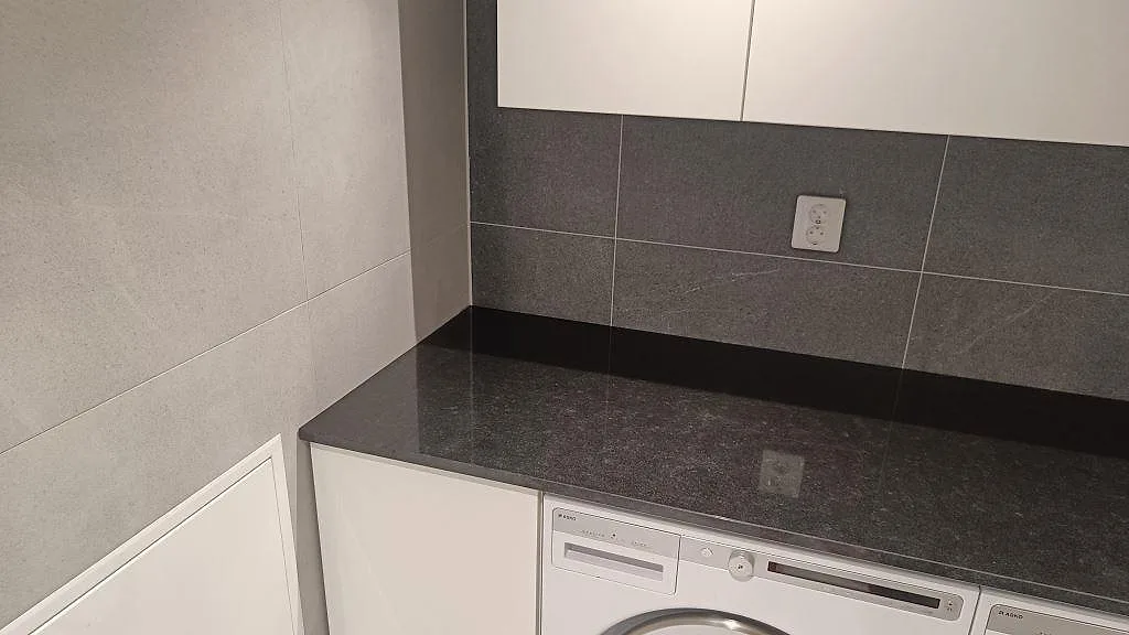 Polerad Nero Assoluto-bänkskiva i svart granit med blank yta, låg stänkkant och vita väggskåp i Kävlinge.