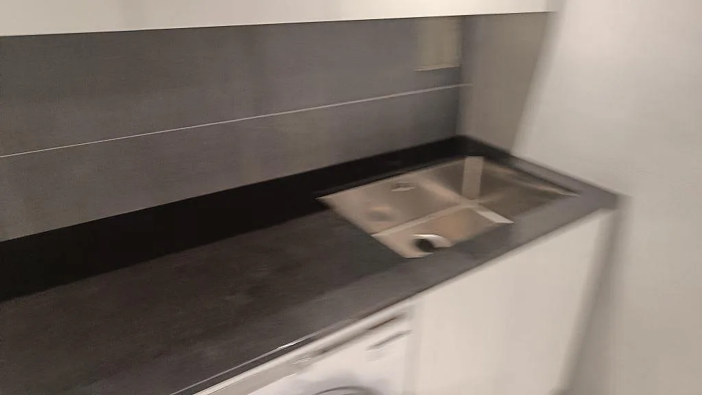 Detaljvy av polerad Nero Assoluto-bänkskiva med rostfri ho, svart stänkkant och kaklad vägg i Kävlinge.