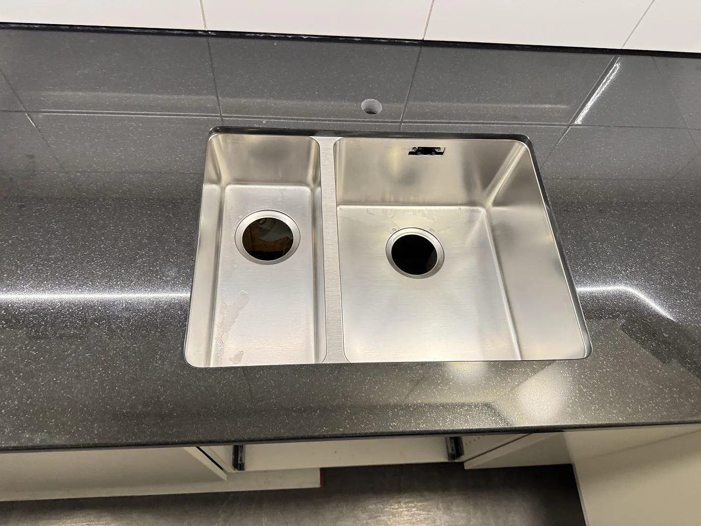 Rostfri dubbelho i en polerad köksbänkskiva av Nero Assoluto granit, fotograferad ovanifrån i ett kök i Karlskrona.
