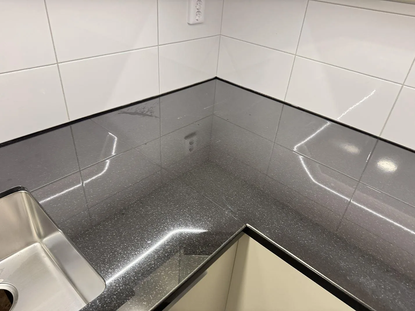Närbild på blank hörnyta i 30 mm Nero Assoluto granit med rostfri diskho vid sidan i köket i Karlskrona.