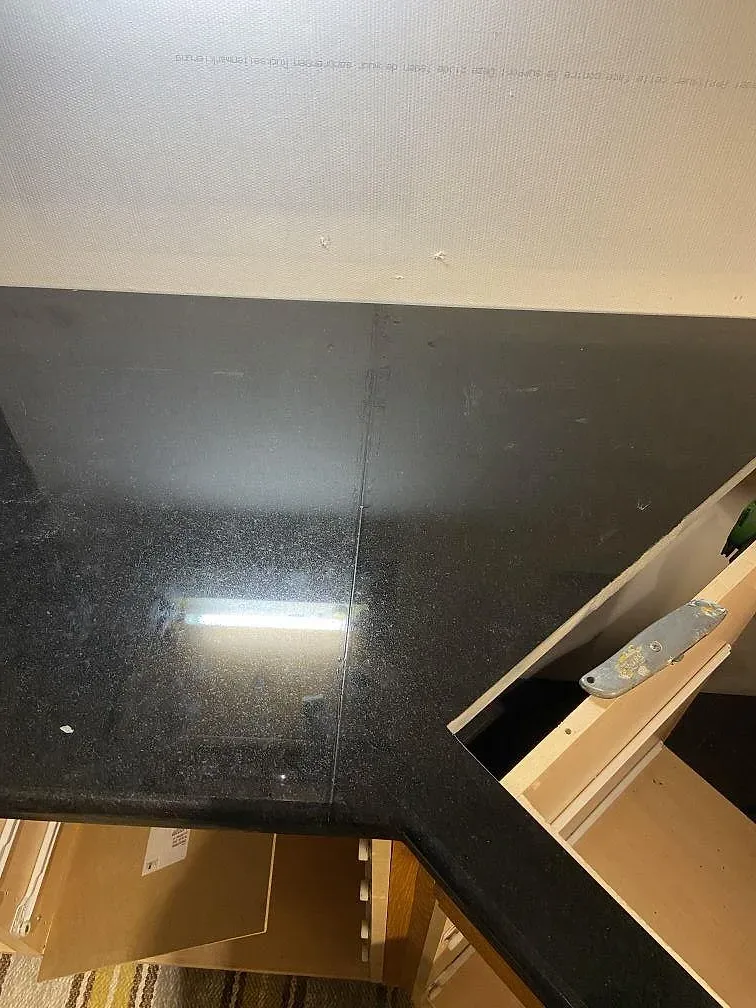 Köksbänkskiva i svart Nero Assoluto granit, polerad, installerad i ett L-format kök med köksö, urtag för diskho och häll under montering i Klagstorp.
