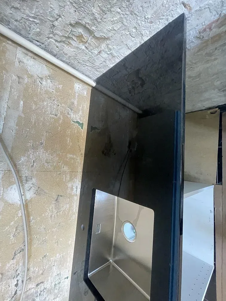 Underlimmad rostfri diskho i polerad Nero Assoluto granitbänk i ett kök under montering i København S.