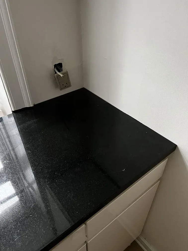 Hörndel av köksbänkskiva i polerad Nero Assoluto granit mot vit vägg i Köpenhamn.