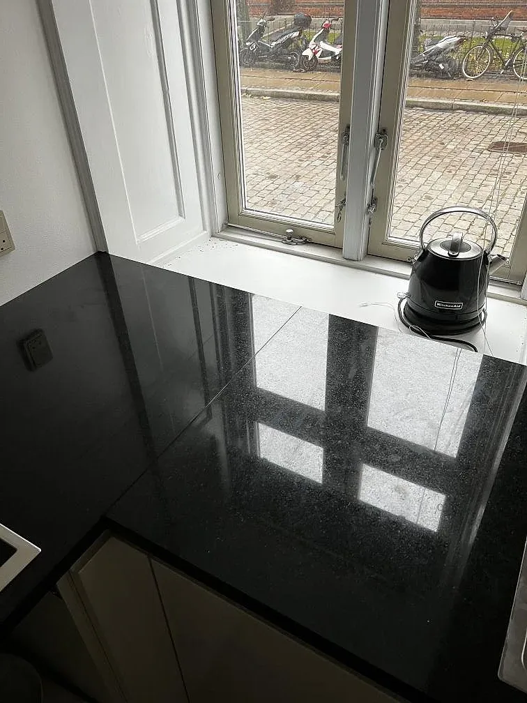 Lång polerad Nero Assoluto granitbänkskiva framför stort fönster i ett kök i Köpenhamn.
