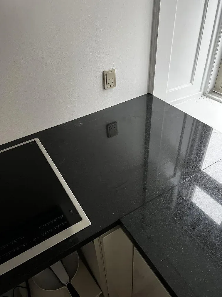 Polerad Nero Assoluto granitbänkskiva med svart induktionshäll och ljusa köksstommar i Köpenhamn.
