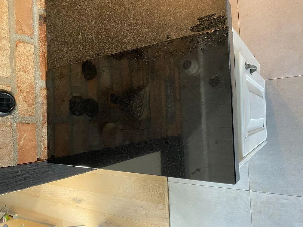 Detalj av polerad Nero Assoluto granit i ett kökshörn med svart blank kant och tegelvägg i Kristianstad.