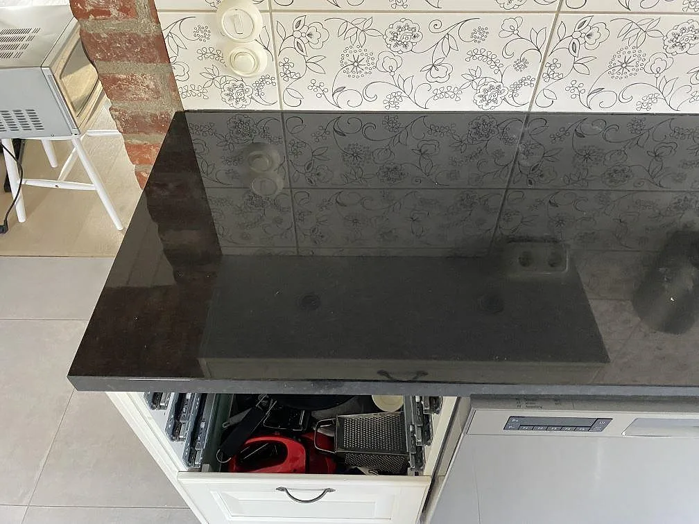 Blank köksbänkskiva i Nero Assoluto granit med reflektioner från kakel och köksskåp i Kristianstad.