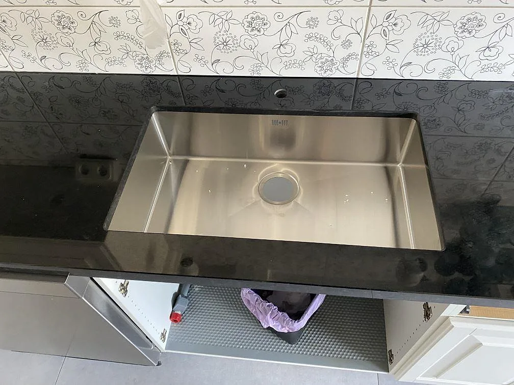 Närbild på rostfri diskho i en polerad köksbänkskiva i Nero Assoluto granit i Kristianstad.