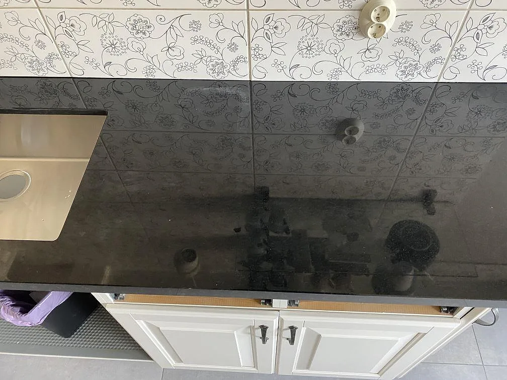 Lång arbetsyta i polerad svart Nero Assoluto granit med vägguttag och öppen köksstomme i Kristianstad.
