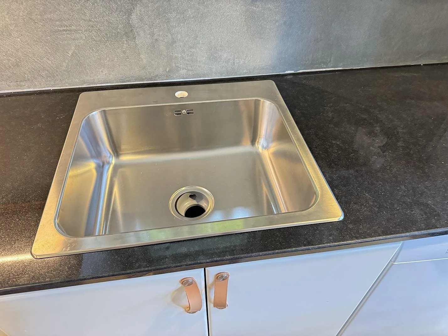Närbild på rostfri diskho ovanpå polerad Nero Assoluto granit i ett kök i Kristianstad.