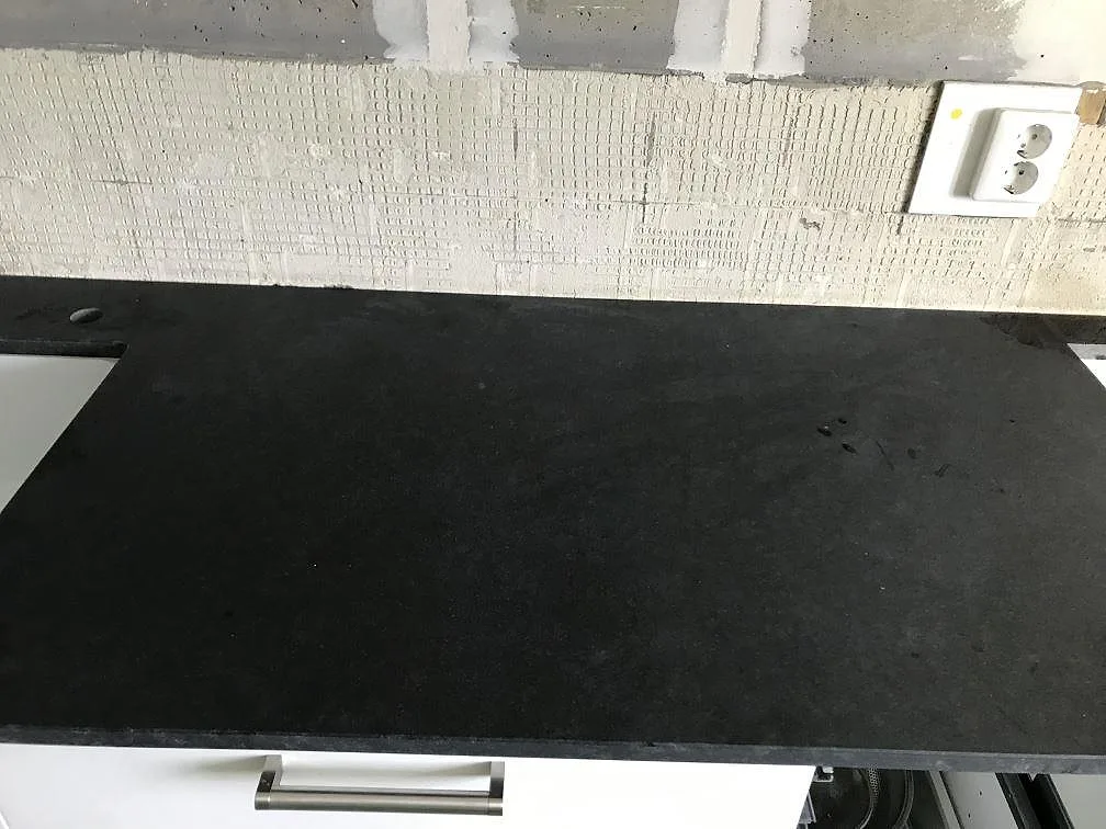 Närbild på den matta svarta Nero Assoluto-graniten i ett kök i Landskrona, där den ljusabsorberande ytan saknar speglingar och ett borrat blandarhål syns vid bakkanten.
