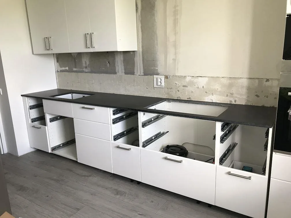 Köksbänkskiva i matt svart Nero Assoluto-granit längs en rak köksrad i Landskrona, fotograferad under montering med urtag för diskho och häll mot oputsad vägg.