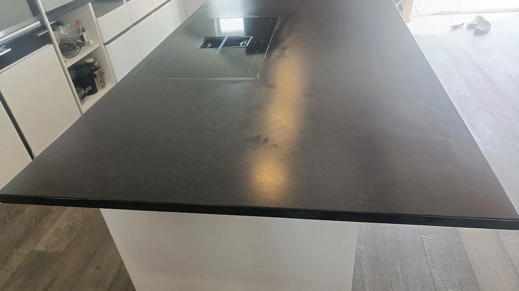 Närbild på matt Nero Assoluto granit som köksö med häll och mörk leather-struktur i Askim.