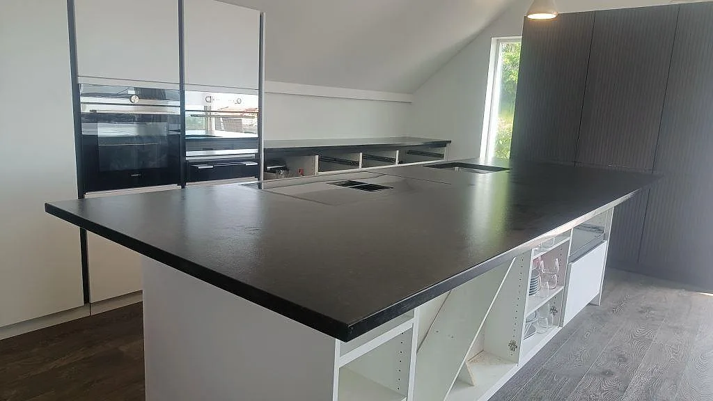 Stor köksö med köksbänkskiva i svart Nero Assoluto granit, matt leather-yta, i ett kök i Askim.