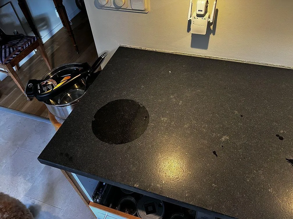 Svart Nero Assoluto Leather bänkskiva med matt granityta och rund mörk monteringsmarkering i ett kök i Höllviken.