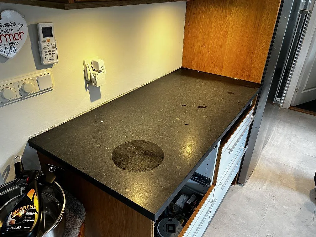 Installerad köksbänkskiva i svart Nero Assoluto Leather granit, matt, med träpanel och vit skåpinredning i Höllviken.