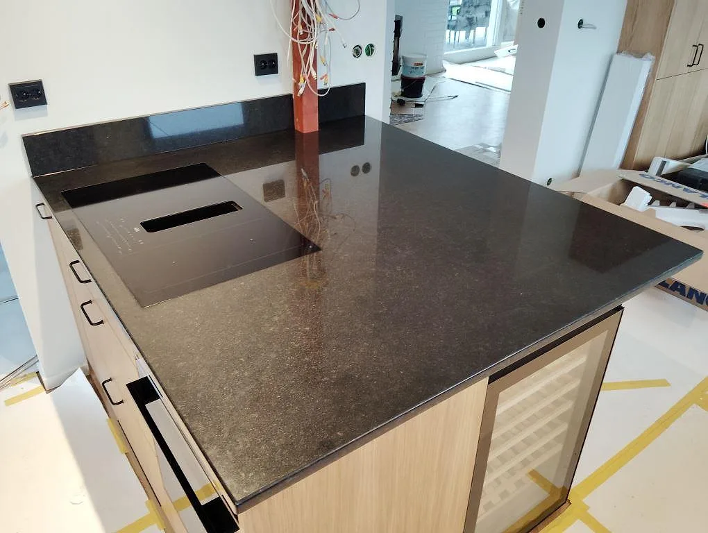 Polerad köksö i svart granit Nero Assoluto med mörk sammanhängande stenyta och träinredning i ett kök i Lidingö.
