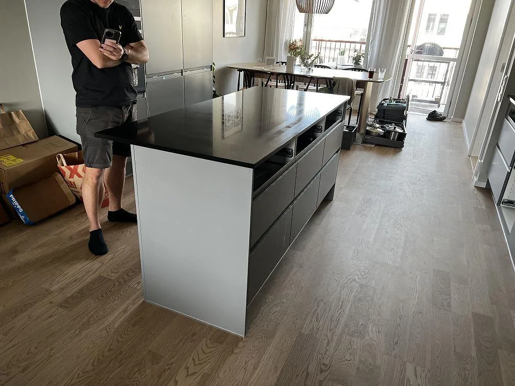 Köksö i matt Nero Assoluto granit monterad i ett öppet kök i Limhamn med ljusa stommar och trägolv.