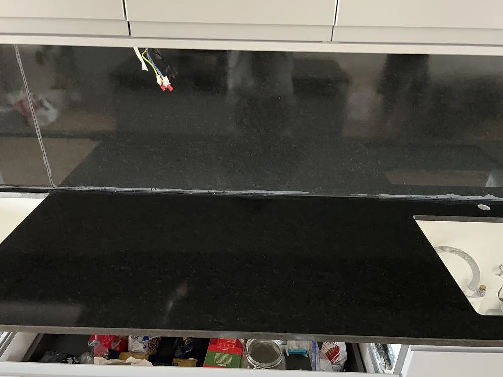Bänkrad i matt Nero Assoluto granit med svart stänkskydd och diskhoöppning under montering i Limhamn.