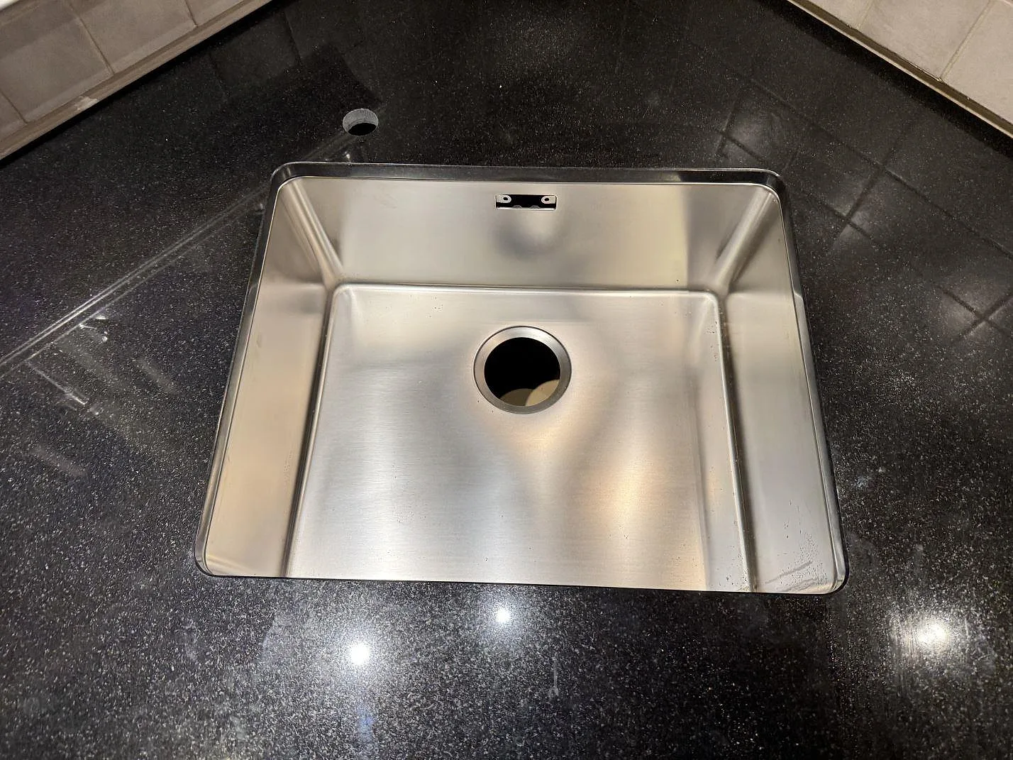 Närbild på rostfri diskho i polerad Nero Assoluto granit som köksbänkskiva i Linneryd.