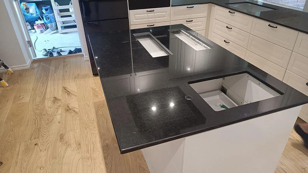 Köksbänkskiva i svart Nero Assoluto granit, polerad, med köksö och utskurna öppningar i Löderup.