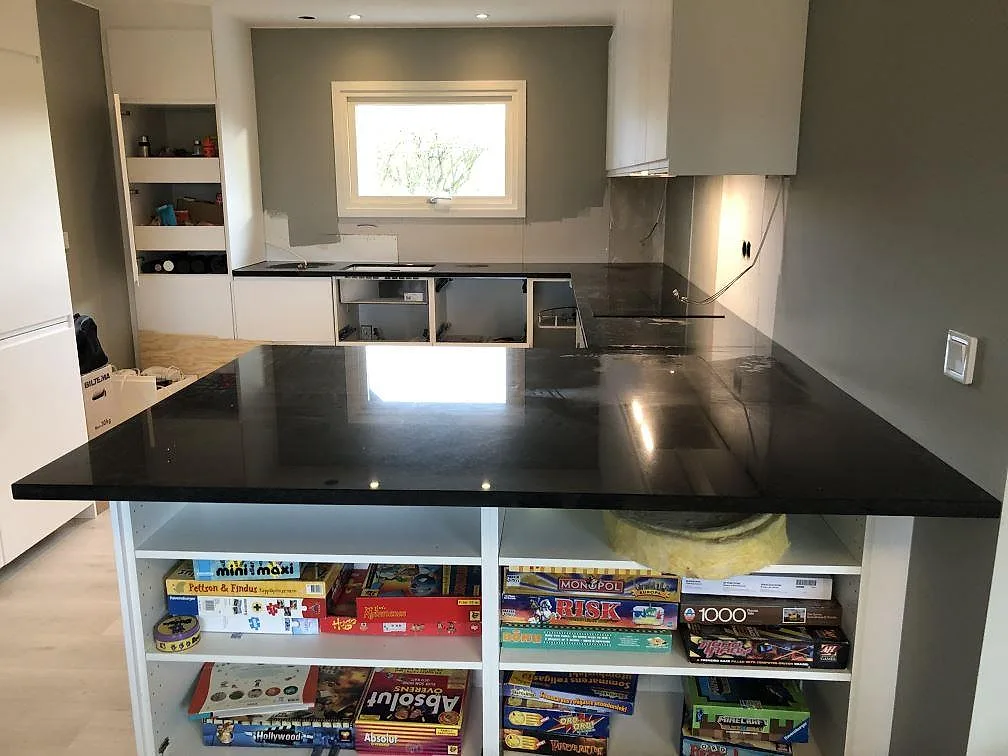 Köksbänkskiva i svart Nero Assoluto granit, polerad, i ett U-format kök med vita luckor i Lomma, fotograferat under montering.