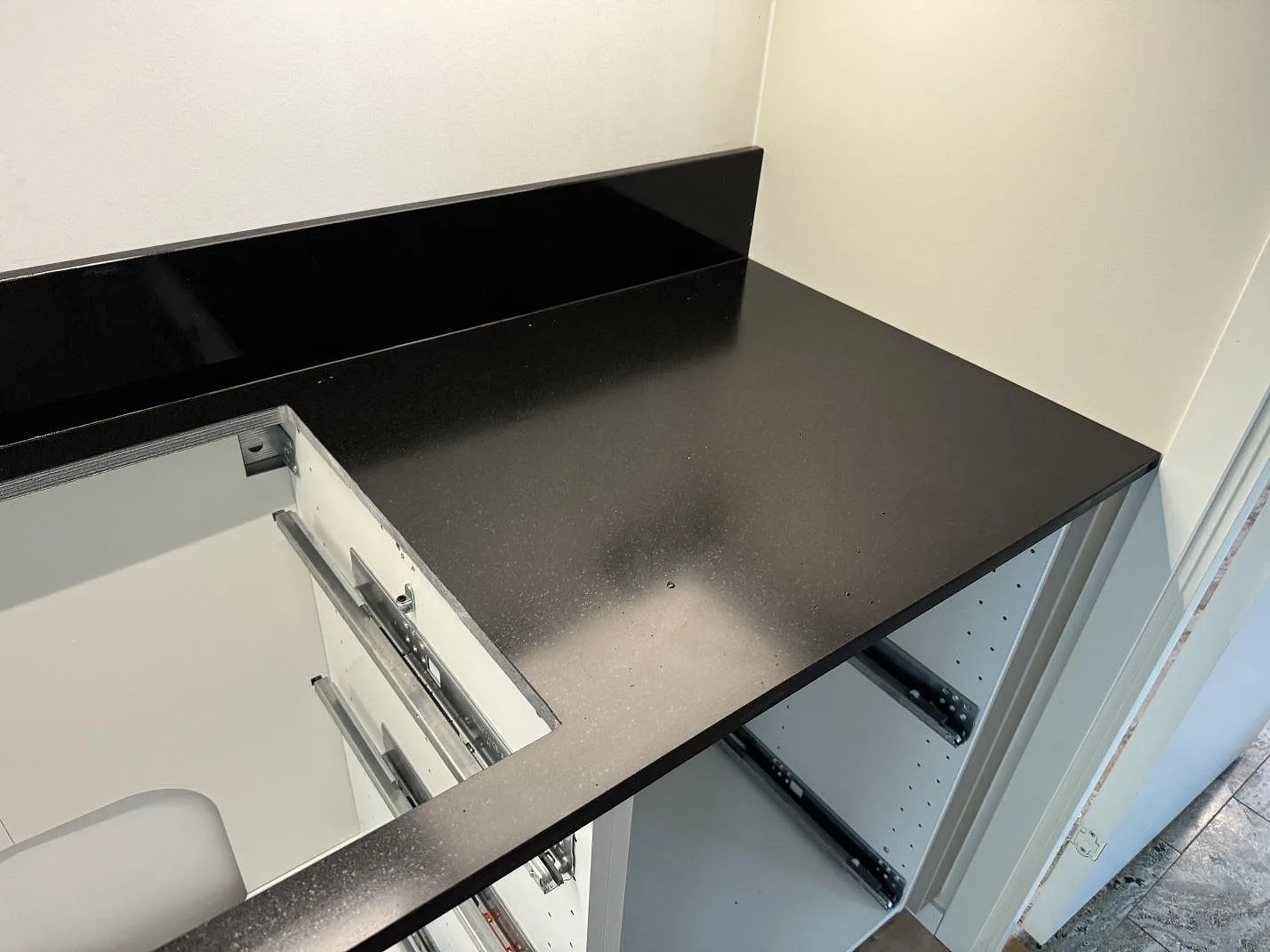 Hörnparti med matt Nero Assoluto granit, låg svart stänkkant och öppna köksstommar i Lomma.