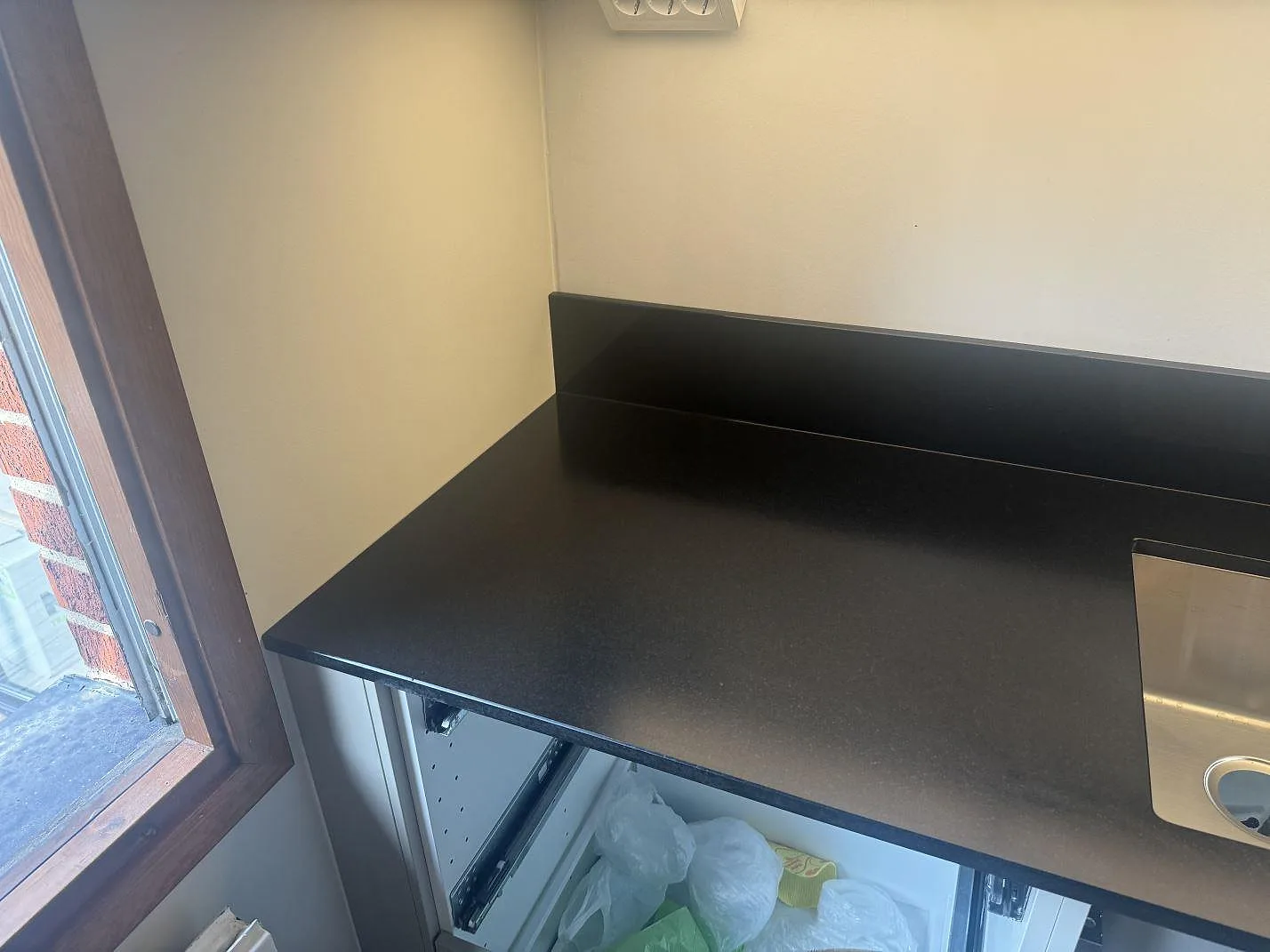 Väggbänk i matt Nero Assoluto granit vid fönster, med låg stänkkant och synlig diskho i Lomma.