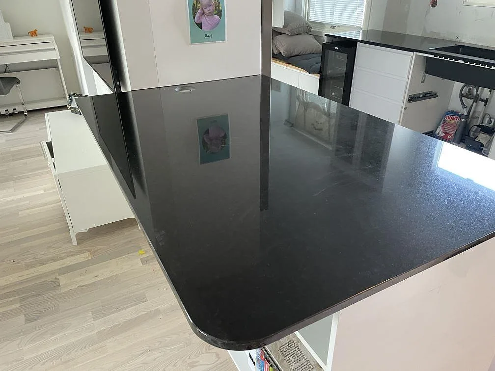 Polerad köksbänkskiva i Nero Assoluto granit med rundad halvö, vita köksstommar och trägolv i Lund.