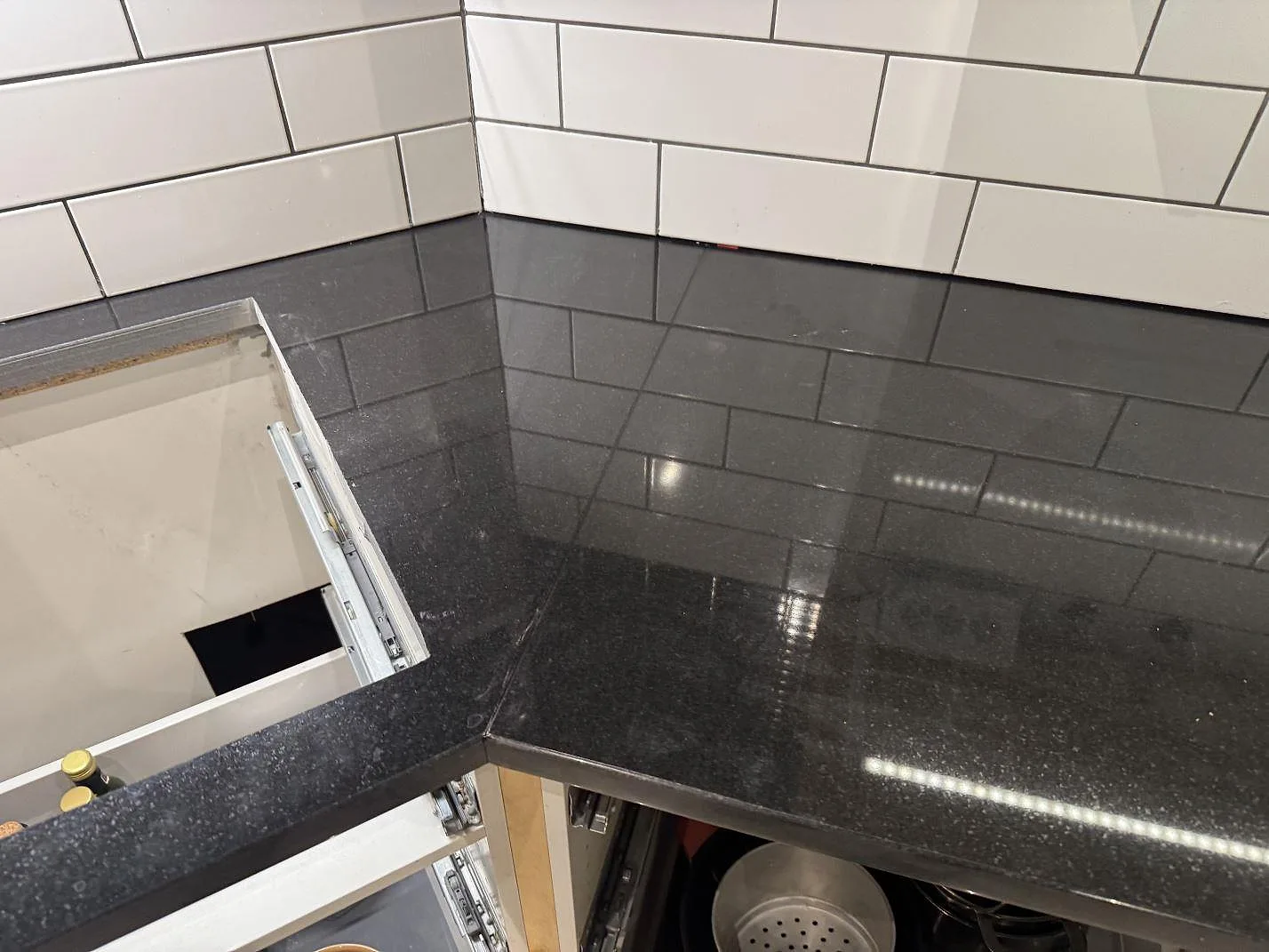 Närbild på blank svart Nero Assoluto-granit som köksbänkskiva i ett hörn mot vitt kakel i Målilla.