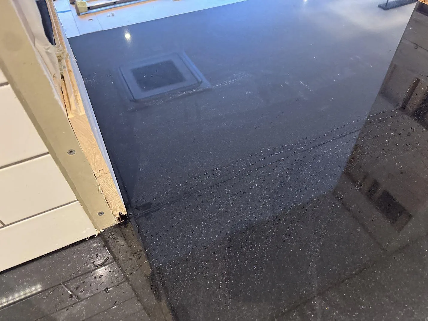 Detalj av polerad svart Nero Assoluto-granit som köksbänkskiva med speglingar och vattenstänk under montering i Målilla.