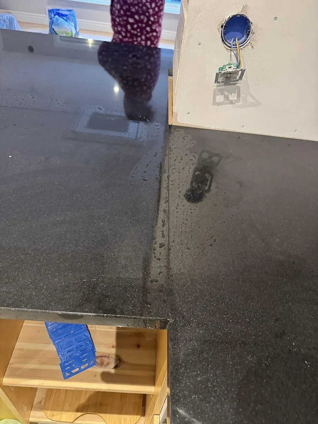 Toppvy av polerad svart Nero Assoluto-granit runt en öppen träförvaring och vägguttag i köket i Målilla.