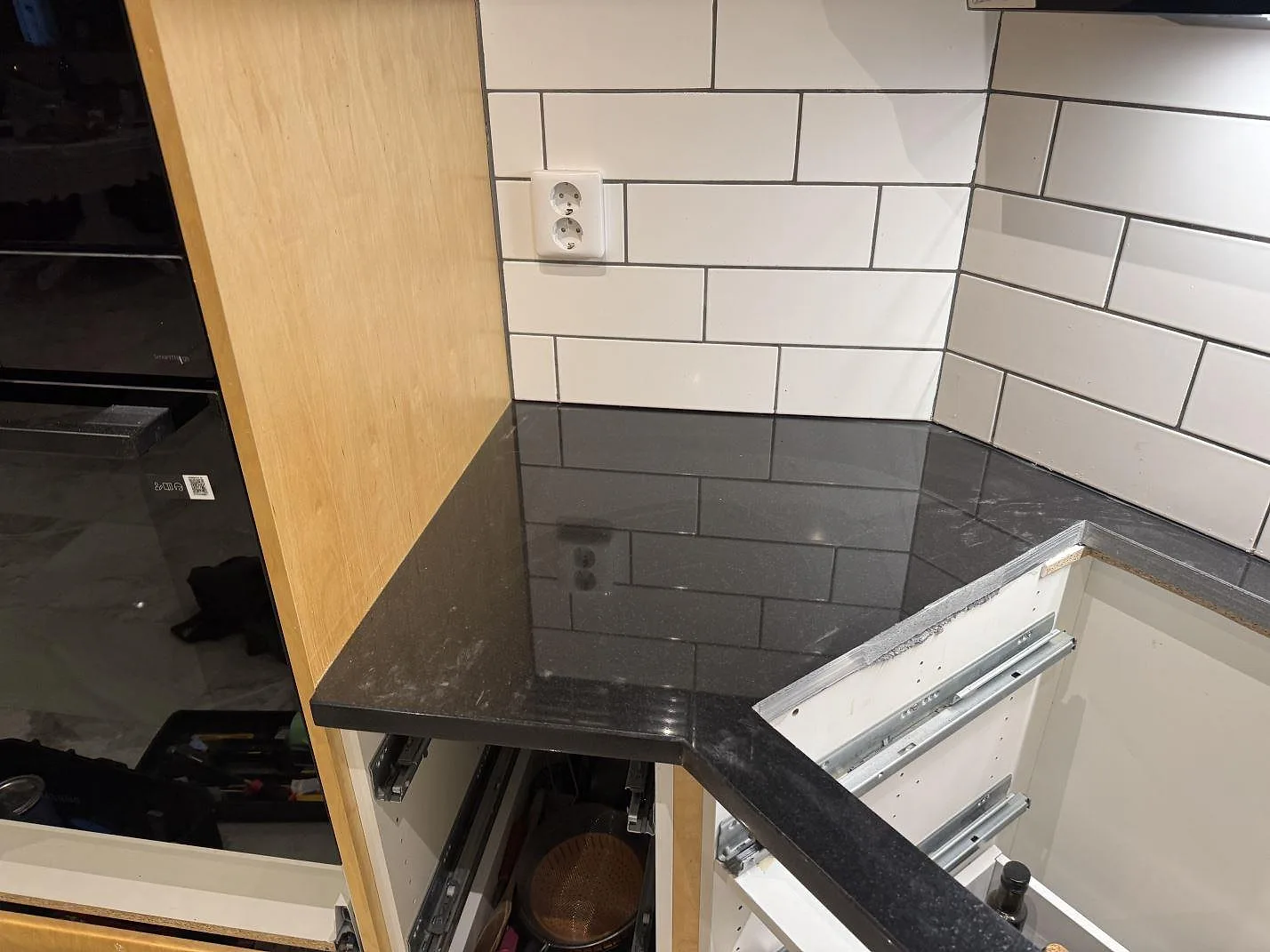 Hörndel av köksbänkskiva i polerad Nero Assoluto-granit mot vitt kakel och träinredning i ett kök i Målilla.