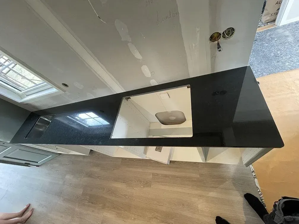 Köksbänkskiva i svart polerad Nero Assoluto-granit med underlimmad rostfri Blanco Andano-diskho och övermonterad häll i ett kök under montering i Malmö.