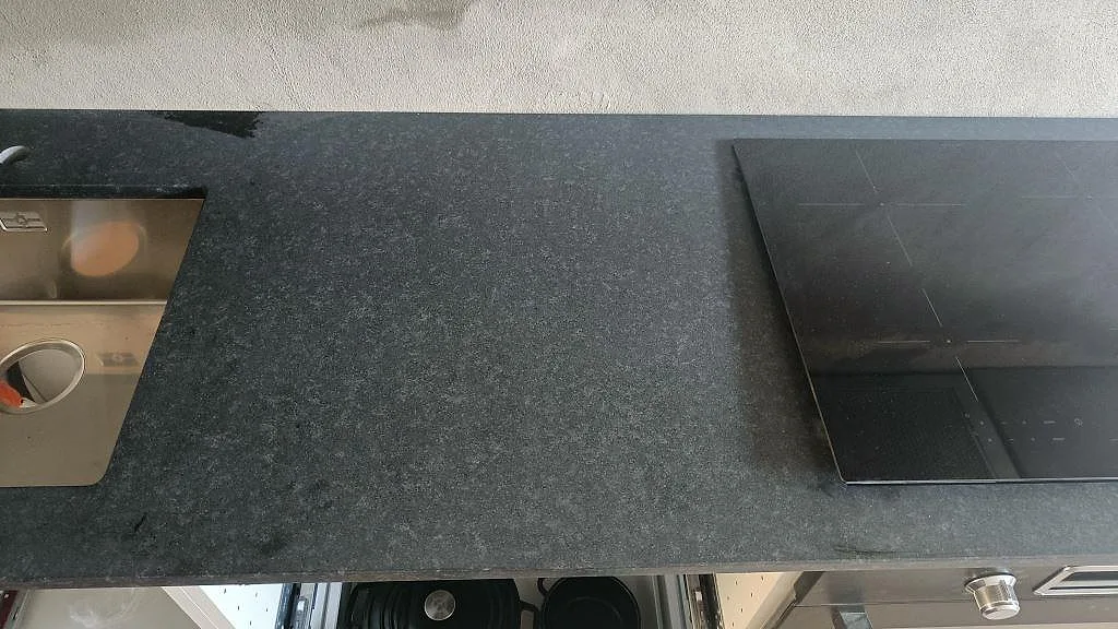 Köksbänkskiva i svart granit Nero Assoluto, matt, med underlimmad rostfri diskho och infälld induktionshäll i ett kök i Malmö.