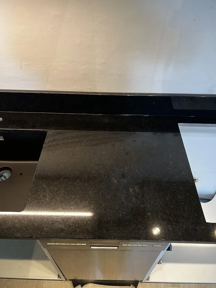 Detalj av Nero Assoluto granit med blank yta, låg stänkkant och rostfri diskho i ett kök i Malmö.