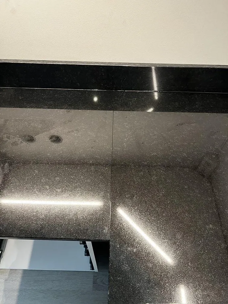 Blank svart Nero Assoluto granit med synlig skarv, ljusreflexer och öppet skåp i kök i Malmö.