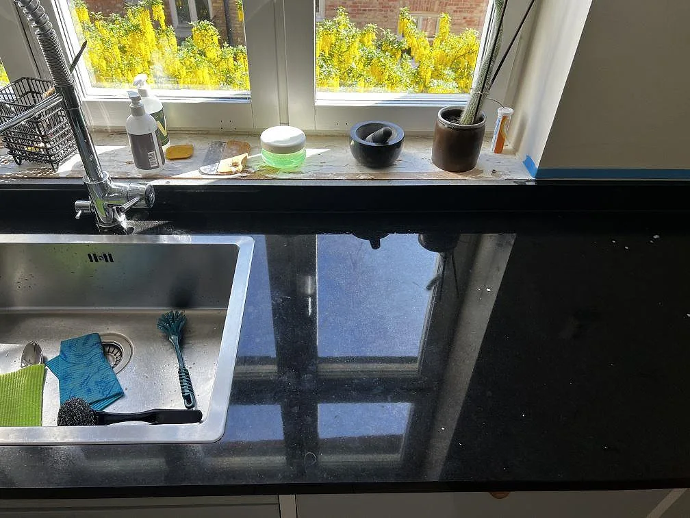 Polerad Nero Assoluto köksbänkskiva i Malmö med rostfri diskho, fönsterljus och svart granitstänkkant.