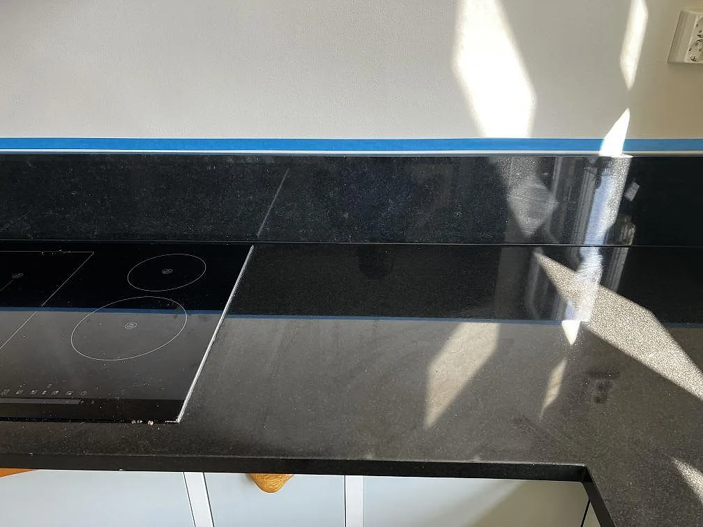 Detalj av polerad Nero Assoluto granit i Malmö med svart induktionshäll, blank yta och stänkkant längs väggen.