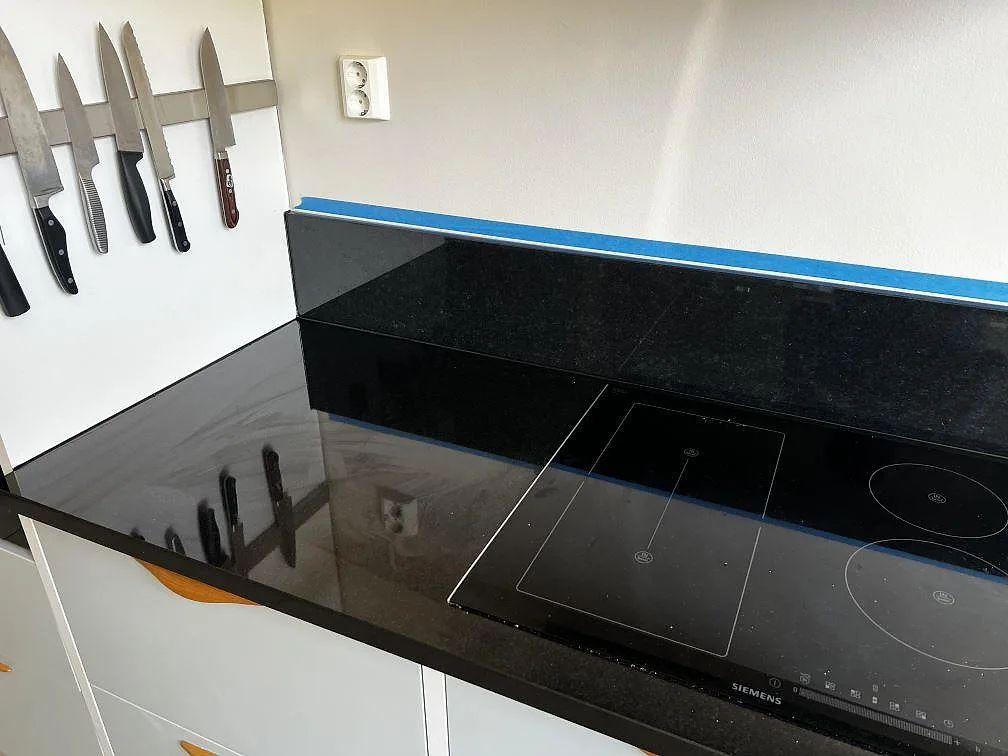 Polerad Nero Assoluto granit som köksbänkskiva i Malmö med svart induktionshäll, låg stänkkant och ljusa skåpsfronter.