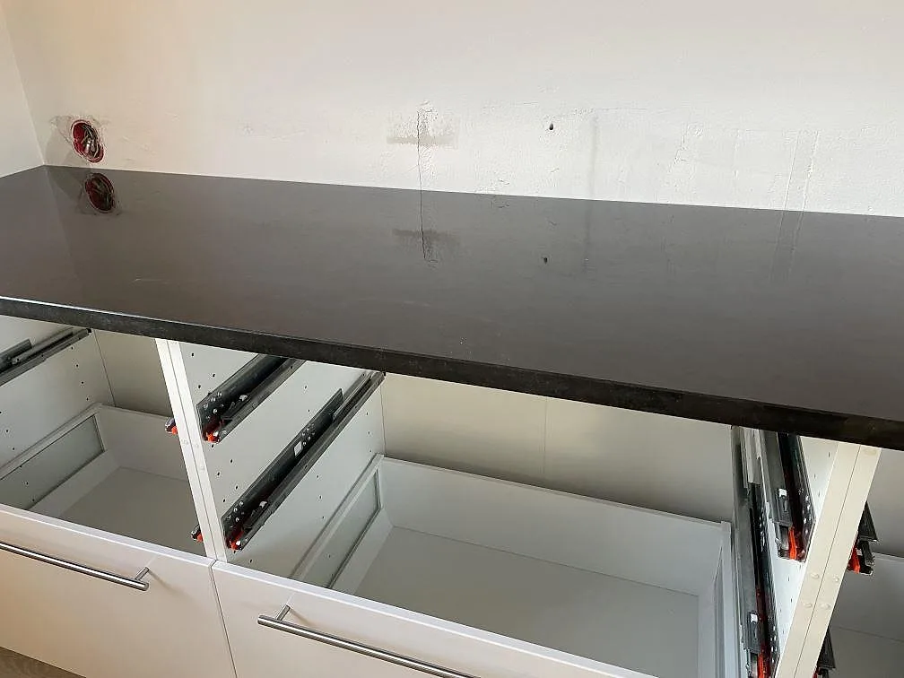 Rak köksbänkskiva i polerad Nero Assoluto granit över öppna lådstommar och vit vägg i Malmö.